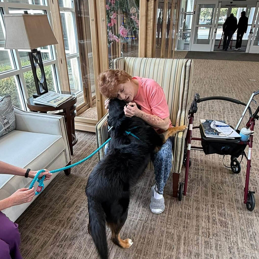 A senior resident in a peach color shirt gives Marlin a hug in a room at the Maimonides Health Center.