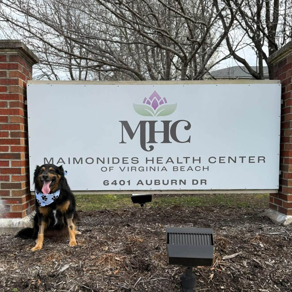 Marlin a black and brown dog sits in front of the MHC sign outside.
