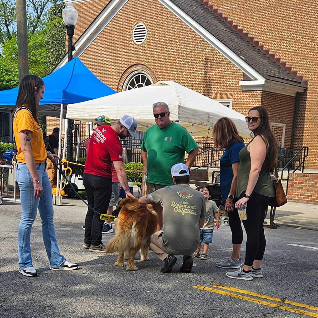 Visitors stop by to pet adoptable pets. Group stands on street in front of white tent.