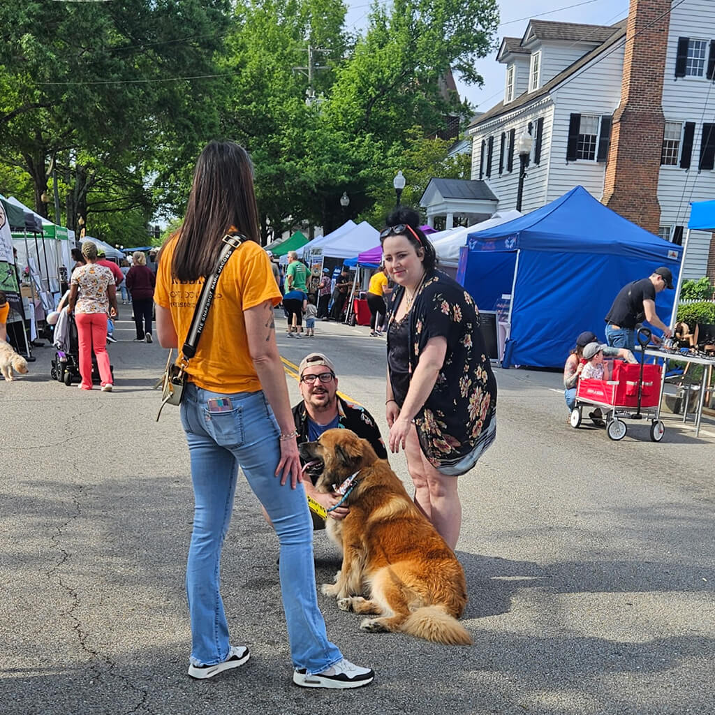 Lady talks to volunteer while petting adoptable dog.