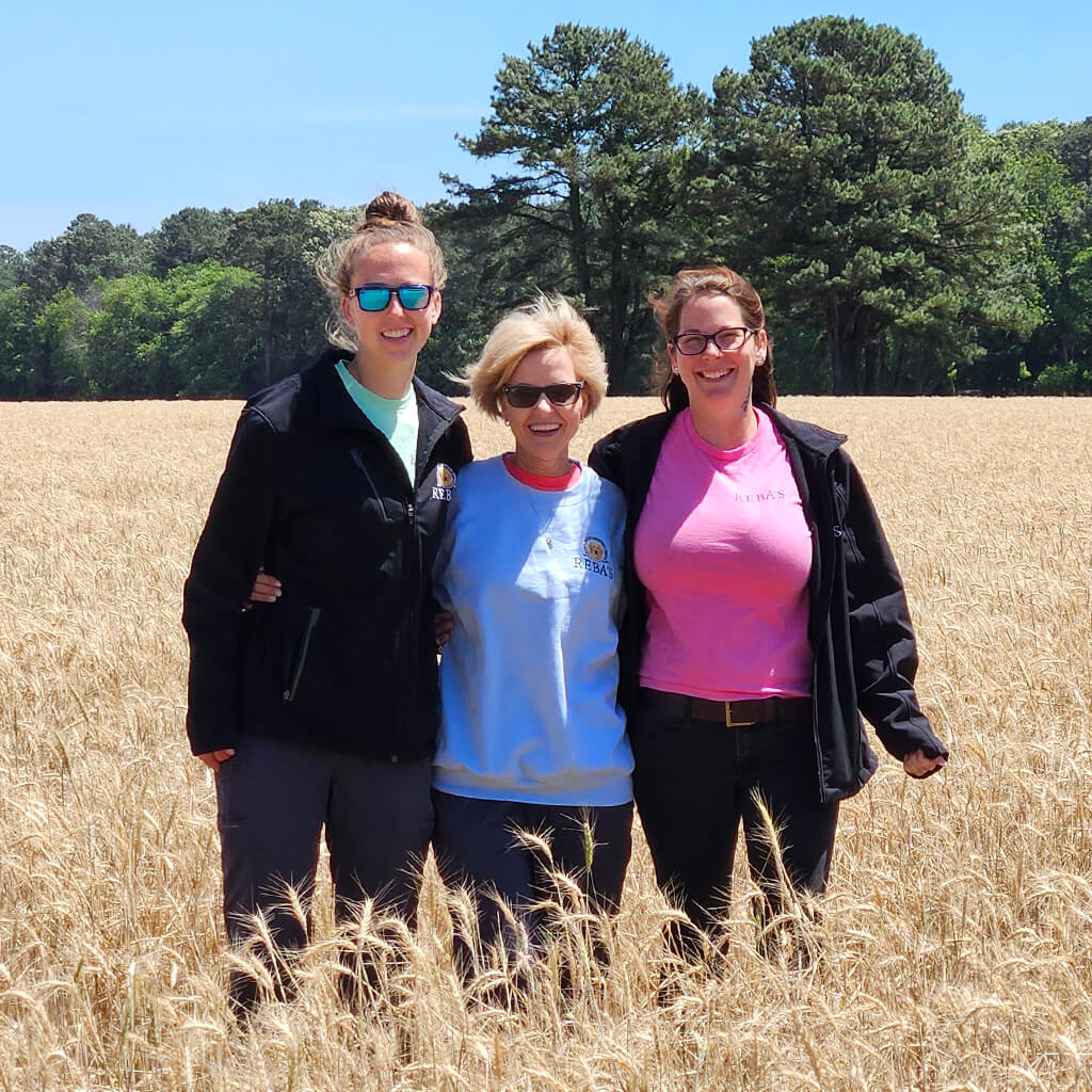 Three team members in a field of wheat with arms around each other.