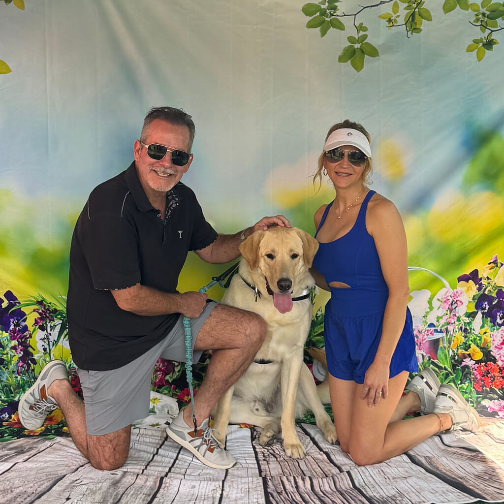 Charlie Daniels kneels next to Bingo a large yellow lab with friend kneeling on a garden type photography background