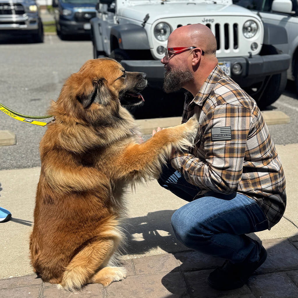 Man in flannel kneeling down next to dog on his hind legs.