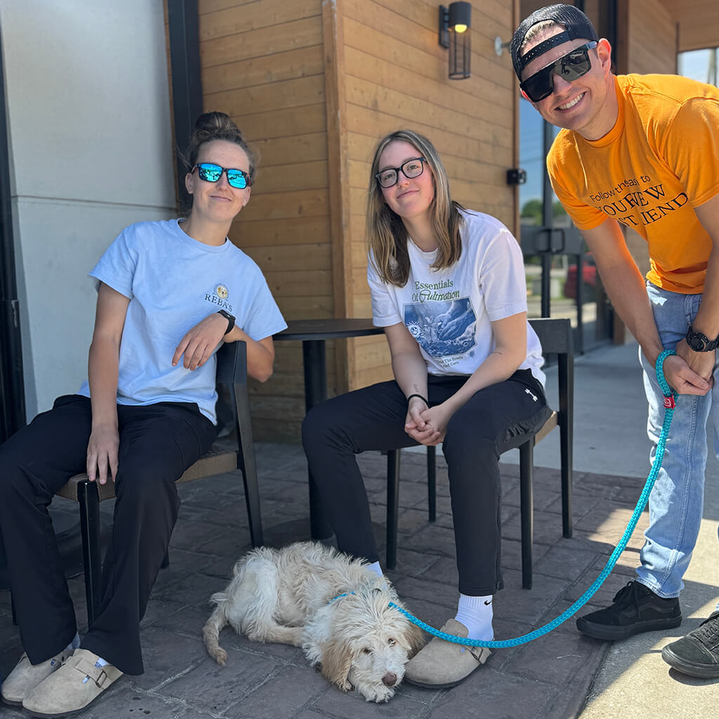 Three volunteers sitting by table and dog laying on the patio.