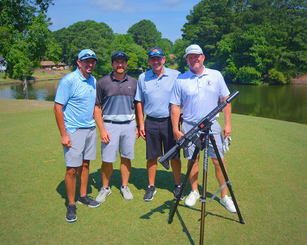 This was team 10. A group of four men standing on the green by the water with trees behind them. The launcher is in front of them.