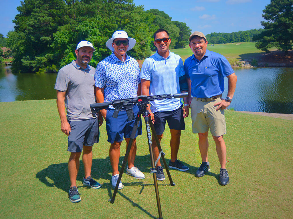 This was team 12. A group of four men standing on the green by the water with trees behind them. The launcher is in front of them.