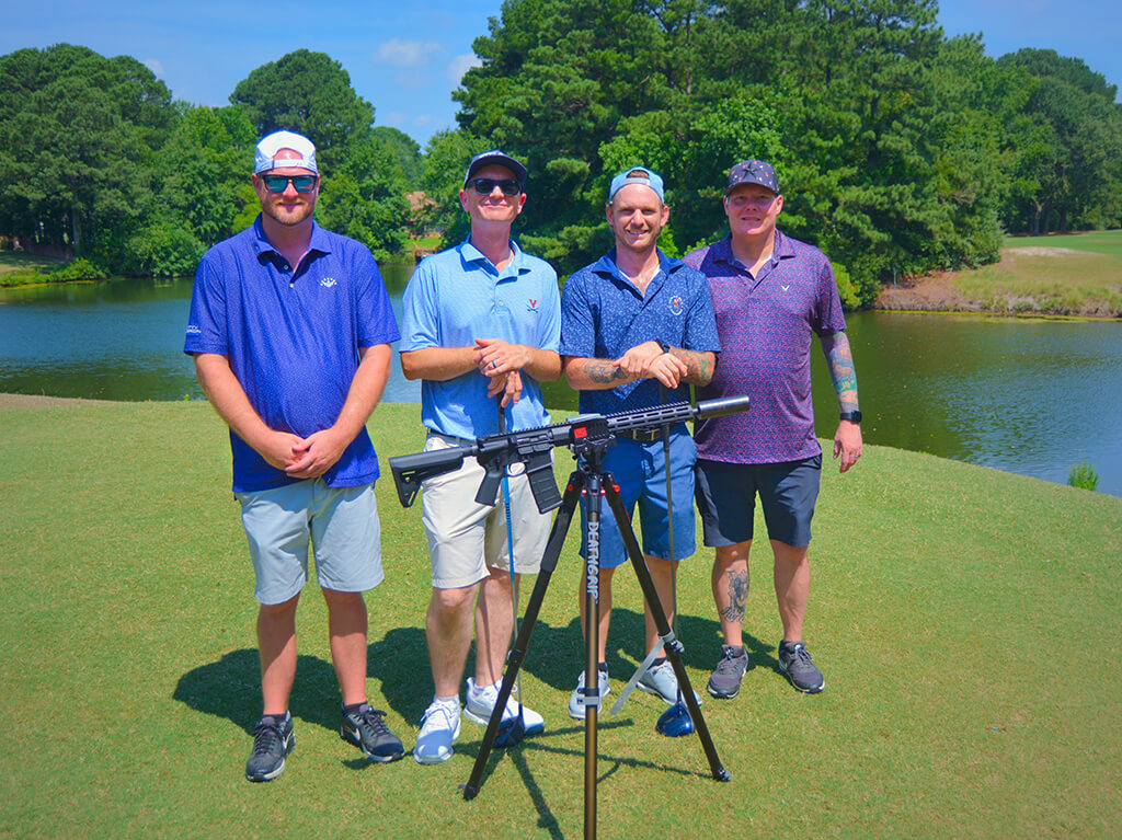 This was team 13. A group of four men standing on the green by the water with trees behind them. The launcher is in front of them.