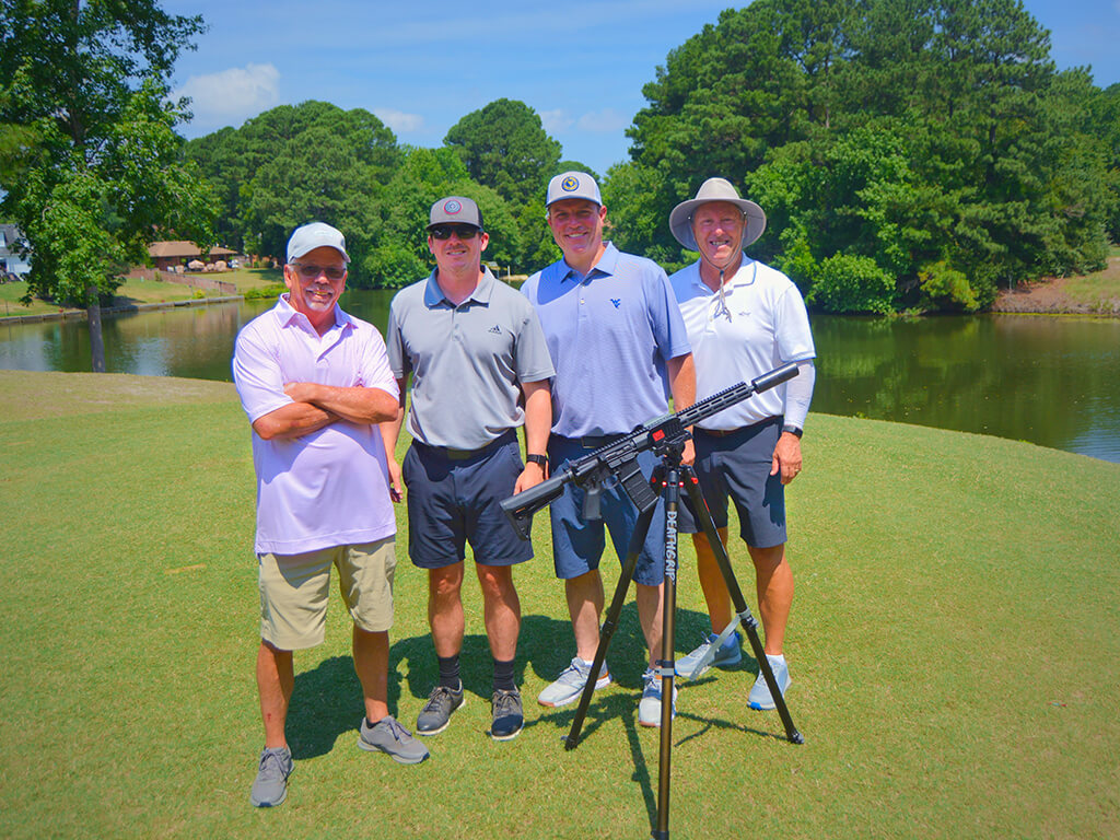 This was team 14. A group of four men standing on the green by the water with trees behind them. The launcher is in front of them.