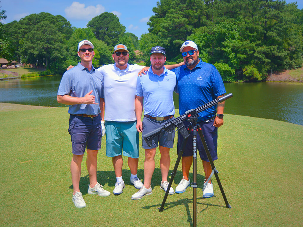 This was team 19. A group of four men standing on the green by the water with trees behind them. The launcher is in front of them.