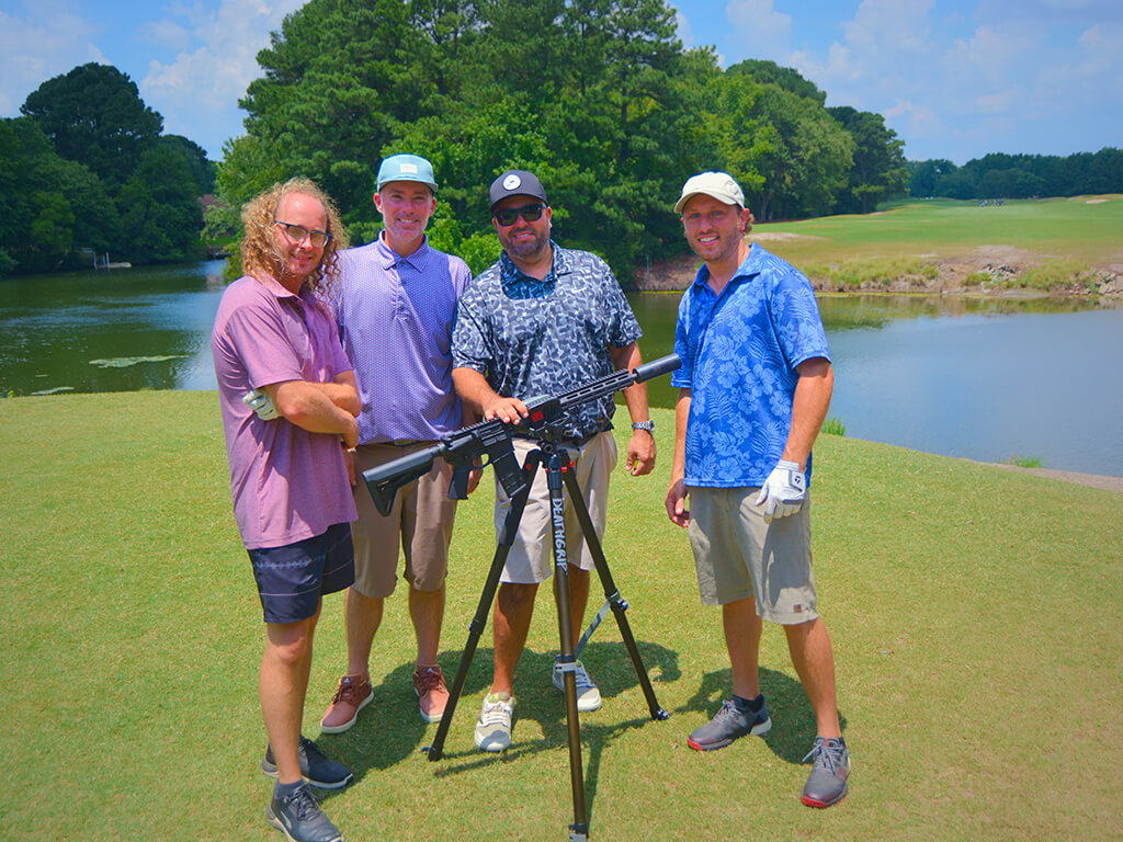 This was team 24. A group of four men standing on the green by the water with trees behind them. The launcher is in front of them. One man has his hand on the launcher.