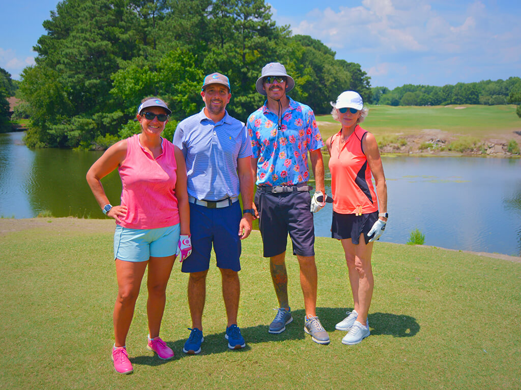 This was team 29. A group of two men and two women standing on the green by the water with trees behind them.