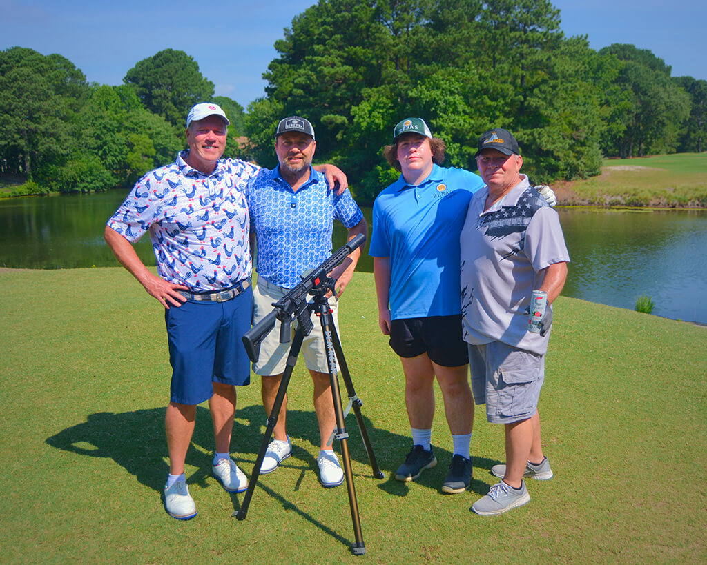 This was team 7. A group of four men with arms on each others shoulders, standing on the green by the water with trees behind them. The launcher is in front of them.