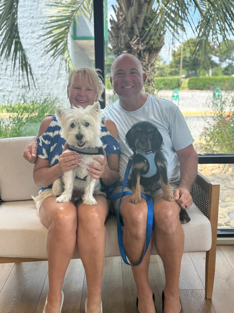 Couple holding 2 dogs, one white dog and one black and brown dog.