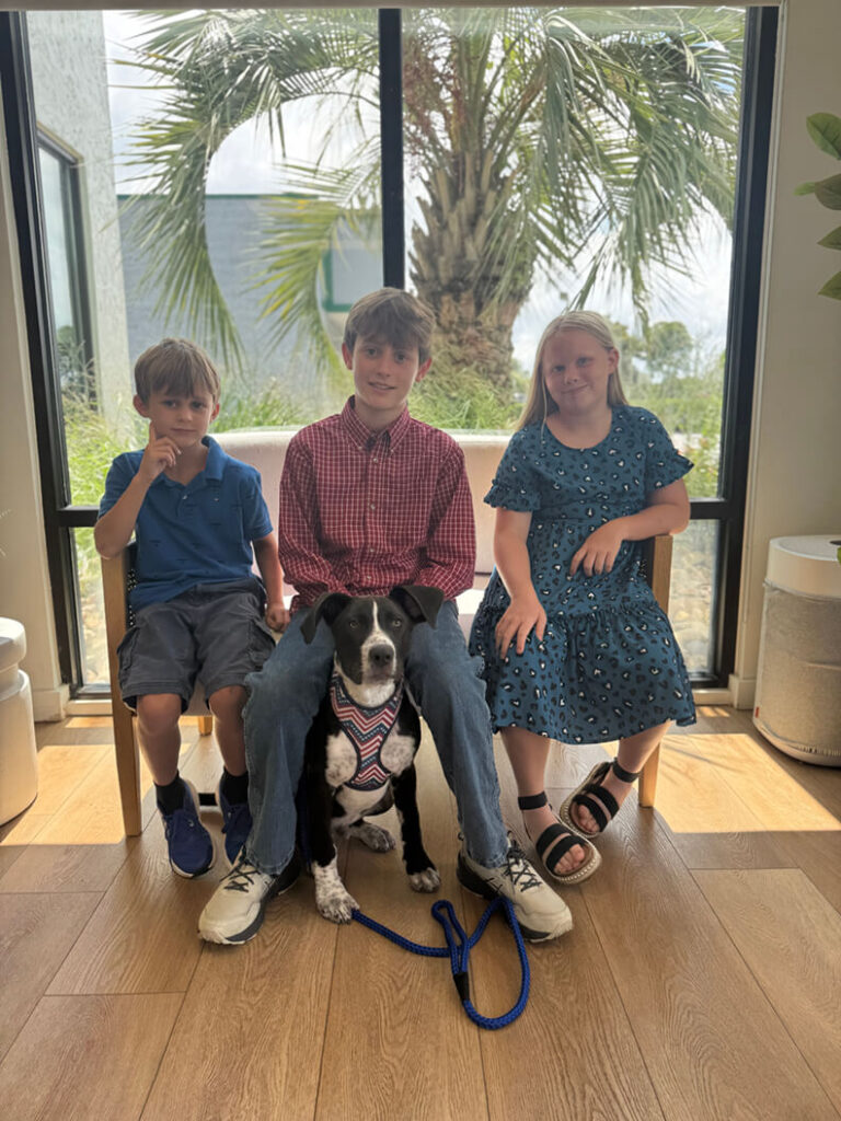 Three young kids sitting with a black and white dog called Pierogi.