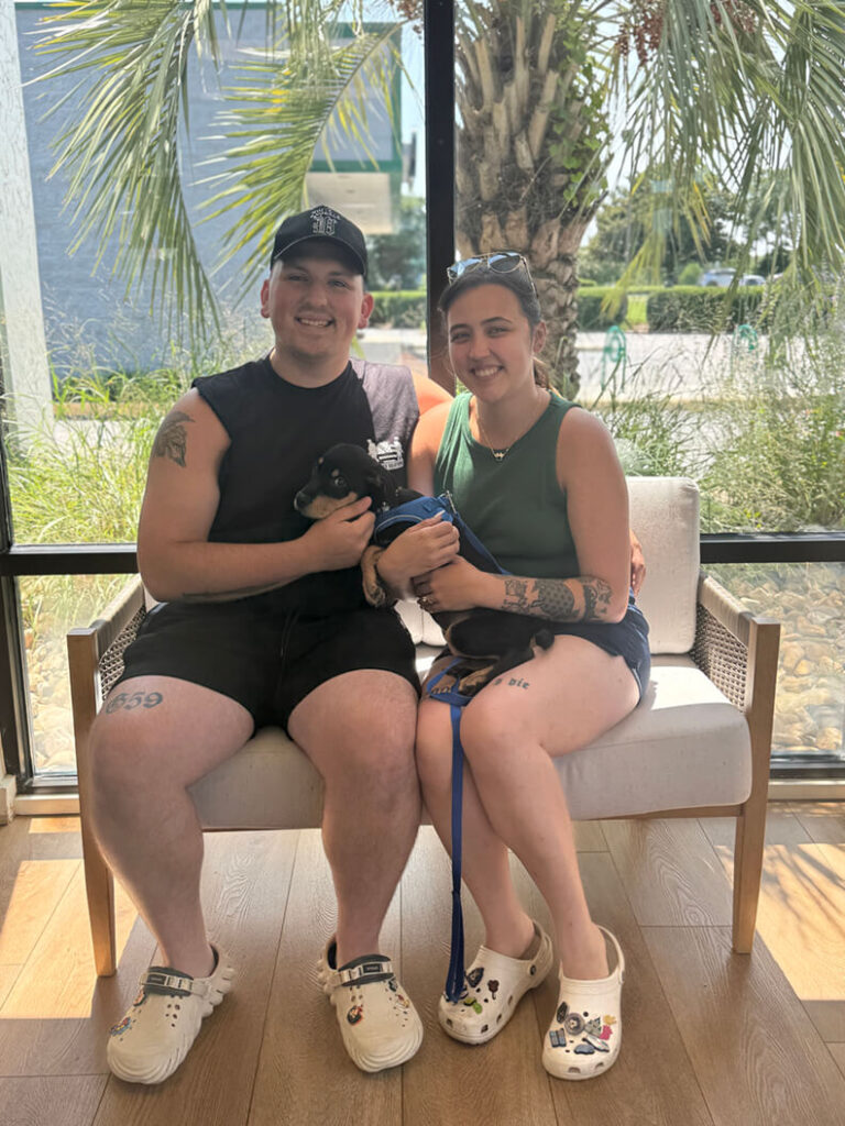 Young couple holding black and brown puppy.