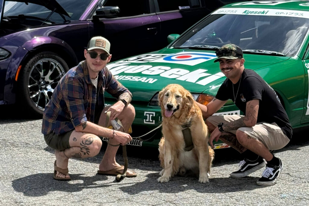 Two men and a dog in front of a green race car