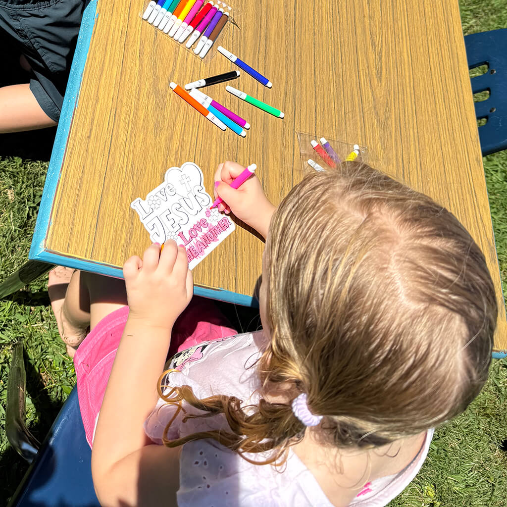 Kids at a table coloring a "Love Jesus, love one another" coloring project.