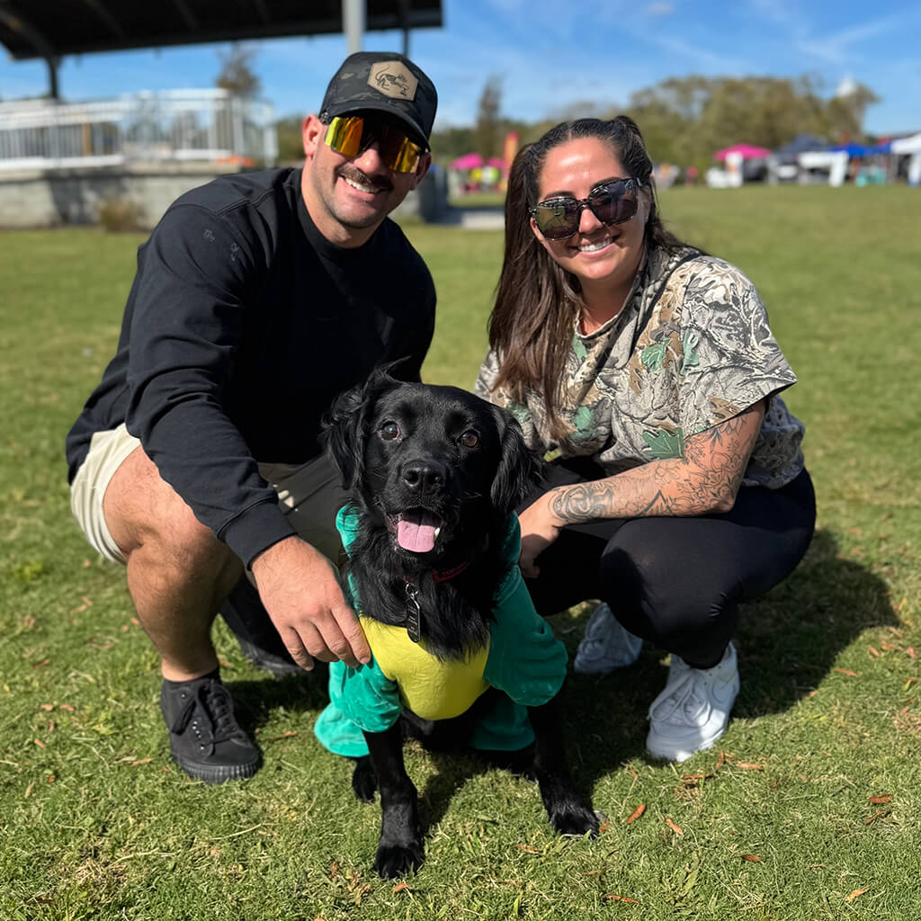 A young couple pose with the black puppy in the lawn.