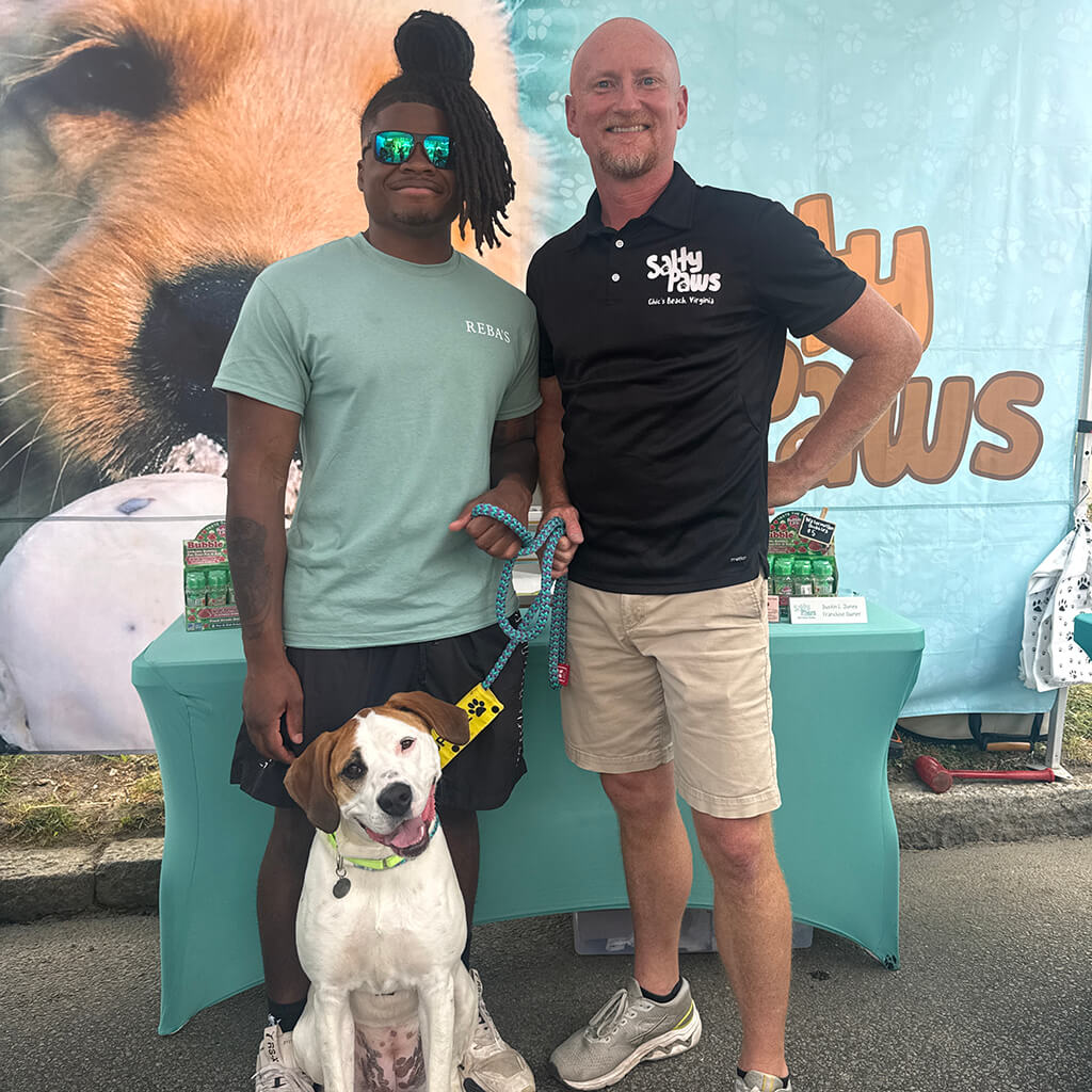 Staff member and Salty Paws vendor pose with white dog with brown ears