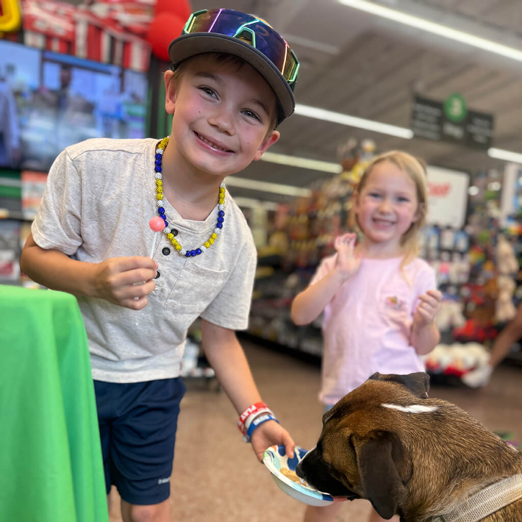 Little kid feeding dog with happy girl in background waving
