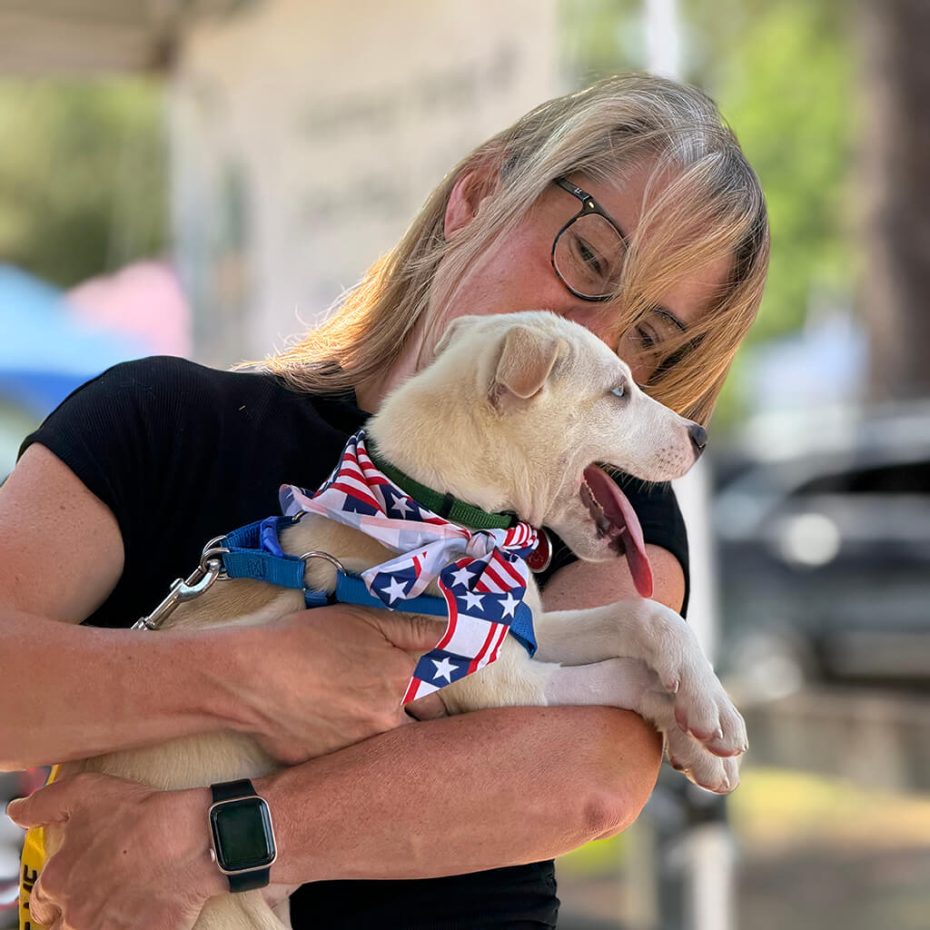 Lady holding the white dog with patriotic bandana